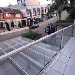 Varanda com piso de cerâmica e guarda-corpo de vidro.