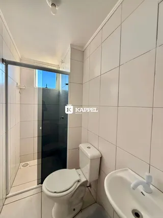 Banheiro com revestimento de azulejos brancos, vaso sanitário e pia.