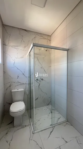 Banheiro com box de vidro e revestimento em mármore claro.
