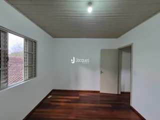 Interior de uma sala com piso de madeira e parede branca.