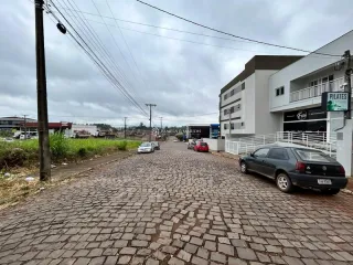 Vista da entrada de uma residência em Lajeado, Brasil, com pavimento de tijolos e edifícios modernos ao fundo.