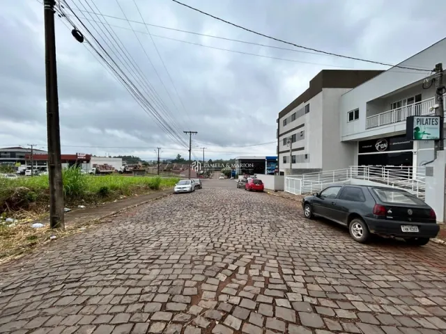 Vista da entrada de uma residência em Lajeado, Brasil, com pavimento de tijolos e edifícios modernos ao fundo.