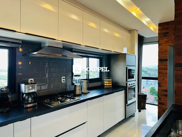 Cozinha moderna com armários brancos e bancadas escuras em um apartamento em Lajeado.