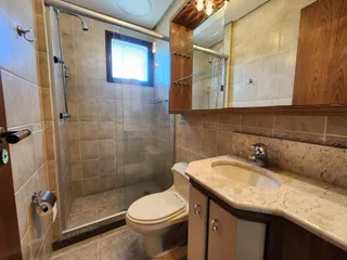 Banheiro com box de vidro, azulejos e bancada de mármore.