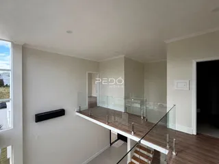 Vista de um ambiente interno com piso de madeira e guarda-corpo de vidro.