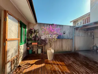 Uma área externa de madeira com plantas adjacente a uma parede clara.