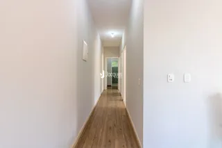 Corredor interno de uma residência com piso de madeira clara.