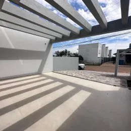 Vista de uma área externa coberta com estrutura de concreto e luz solar.