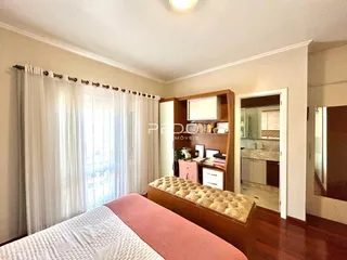 Quarto com piso de madeira e janela com cortinas brancas.