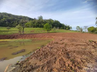 Paisagem de terra vermelha com água no primeiro plano em uma área externa.