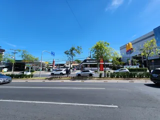 Vista externa de uma rua com veículos e estabelecimentos comerciais em Lajeado.