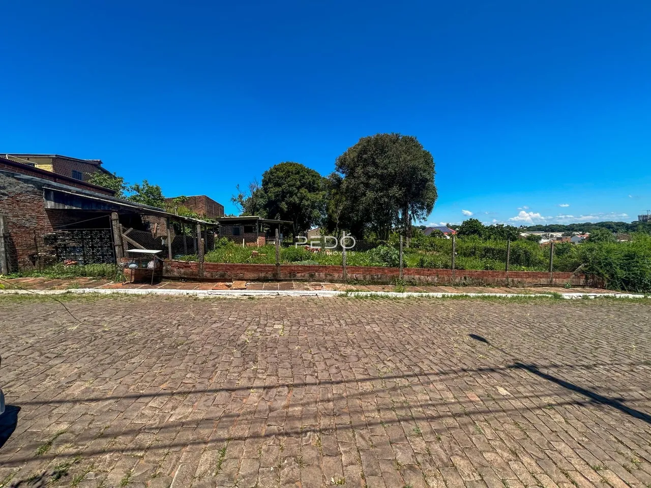 Vista externa do terreno com muro de tijolos e pavimento de paralelepípedos.