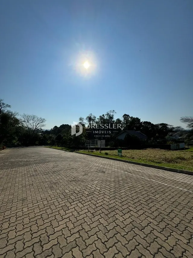 Vista da fachada de uma propriedade com área pavimentada e vegetação ao fundo.