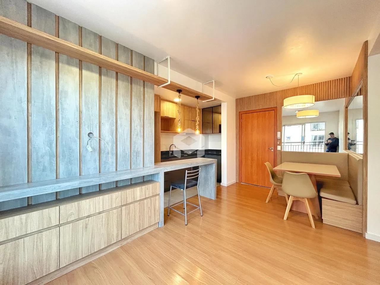 Ambiente interno de uma sala de estar com piso de madeira clara e bancada de cozinha.