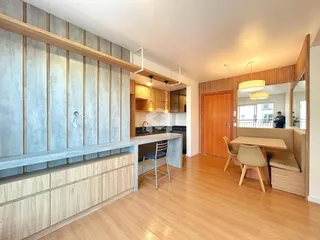 Ambiente interno de uma sala de estar com piso de madeira clara e bancada de cozinha.