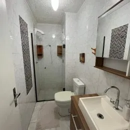 Banheiro com revestimento branco e box de chuveiro.