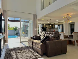 Sala de estar com sofá de couro marrom e acesso a uma área externa com piscina.