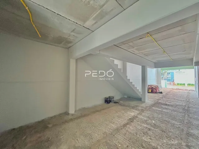 Vista interna de uma estrutura em construção com paredes brancas e teto de concreto exposto.