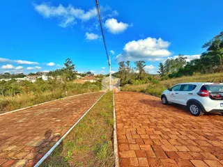 Vista externa de uma propriedade com pavimento de tijolos e vegetação ao fundo.