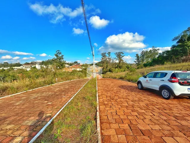 Vista externa de uma propriedade com pavimento de tijolos e vegetação ao fundo.