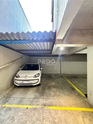Vista externa de uma garagem ou pátio com um carro estacionado sob uma estrutura de telhado.