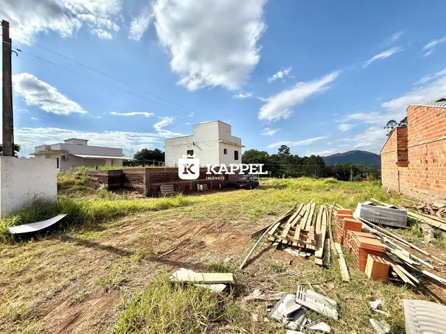 Vista externa de uma casa branca com terreno e materiais de construção no primeiro plano.