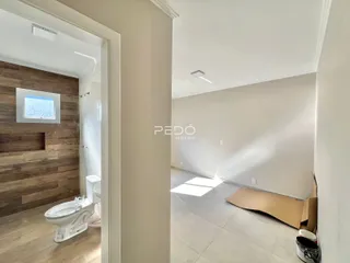 Vista interna de um corredor com acesso a um banheiro e uma sala ampla.