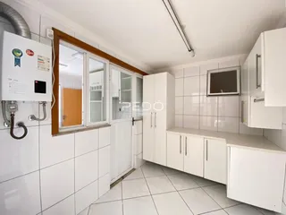 Interior de uma cozinha com armários brancos e piso de cerâmica.