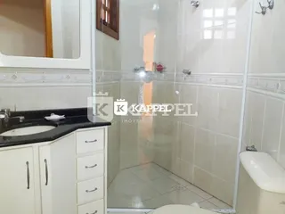 Interior de um banheiro com revestimento branco e box de vidro transparente.