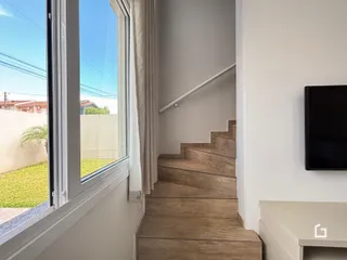 Hall com escadas de madeira e uma grande janela na área interna.