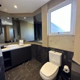 Foto interna de um banheiro com revestimento escuro e vaso sanitário branco.