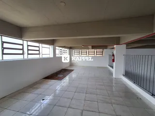Vista interna de um ambiente amplo com piso de cerâmica e grandes janelas.