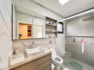 Banheiro moderno com bancada de mármore e box de vidro transparente.