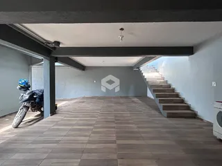 Vista interna de um espaço com piso de madeira e estrutura de concreto aparente.