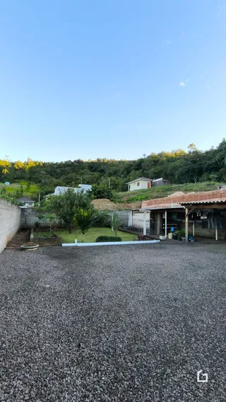 Área externa com terreno coberto por cascalho e vegetação ao fundo.