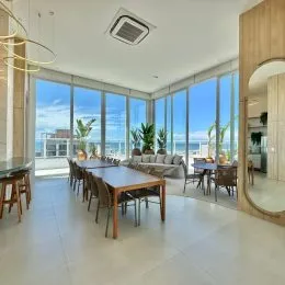Sala de jantar com vista para o mar, apresentando grandes janelas.