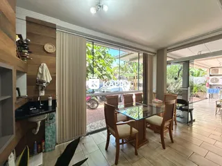 Sala de jantar com mesa de vidro e cadeiras de madeira, com vista para a vegetação externa.