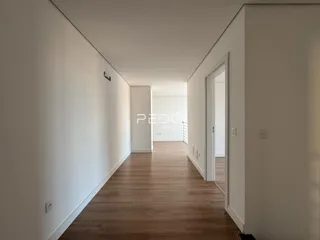 Corredor interno de uma residência com piso de madeira clara.