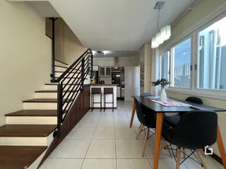 Interior de uma sala de estar com escadaria e área de jantar em um imóvel no Brasil.