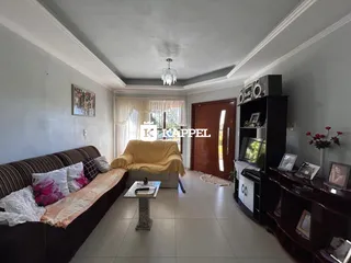 Sala de estar com sofá marrom e poltrona amarela, com janelas cobertas por cortinas claras.