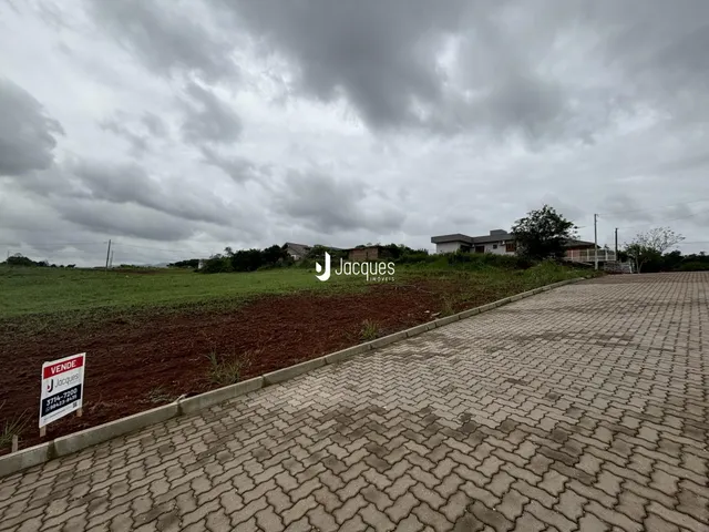 A foto mostra a fachada de uma propriedade com um campo aberto e uma estrada de paralelepípedos.