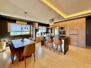 Sala de jantar com mesa de madeira e ilha de cozinha em um ambiente moderno.