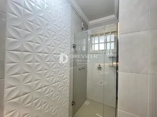 Interior de um banheiro com revestimento de azulejos brancos e box de vidro.