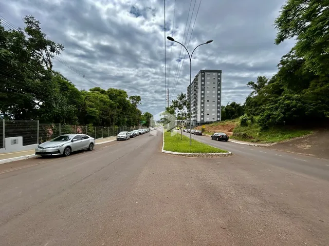 Vista de uma rua arborizada com um prédio residencial ao fundo.