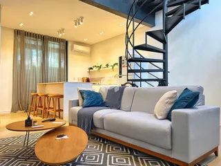 Sala de estar moderna com sofá cinza e escadaria de metal em um apartamento.
