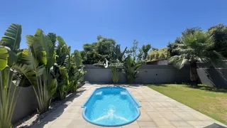 Piscina externa com paisagismo e vegetação ao fundo.