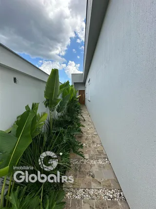 Vista externa de um caminho pavimentado ao lado de uma parede branca com vegetação.