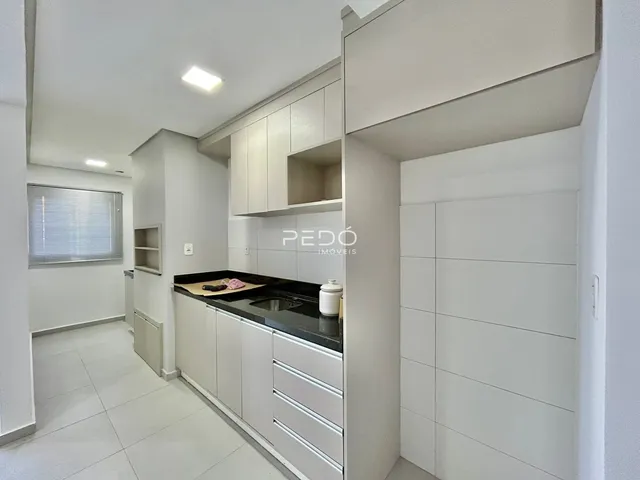 Vista interna de uma cozinha moderna com armários brancos e piso claro.