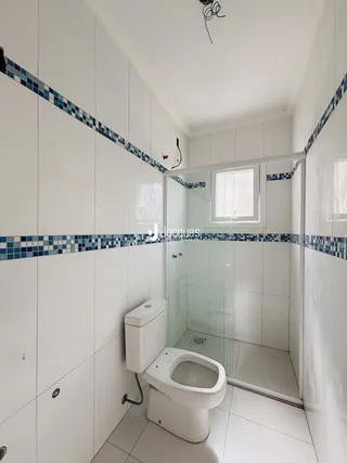 Foto de um banheiro com revestimento cerâmico branco e detalhes em azul.