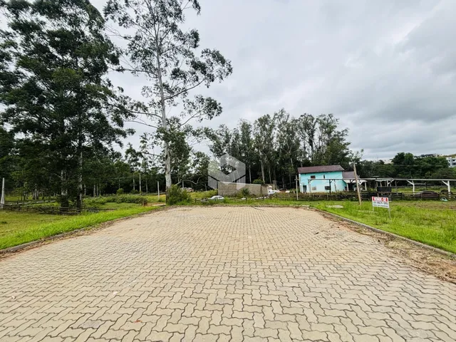 Vista externa do terreno com área pavimentada e vegetação ao fundo.